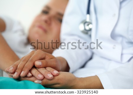 Friendly female doctor hands holding patient hand lying in bed for encouragement, empathy, cheering and support while medical examination. Bad news lessening, compassion, trust and ethics concept Royalty-Free Stock Photo #323925140