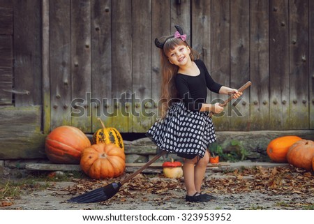 Shot of a little girl in halloween costume posing with broom and pumpkins during Halloween party