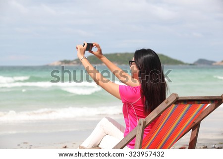 Woman taking photo with cellphone on the beach on spring. Happy girl on vacation taking picture on sea background.