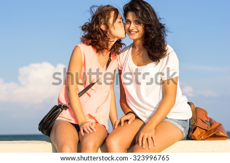 kiss between friends sitting on a low wall - caucasian girls - people, friendship and lifestyle concept