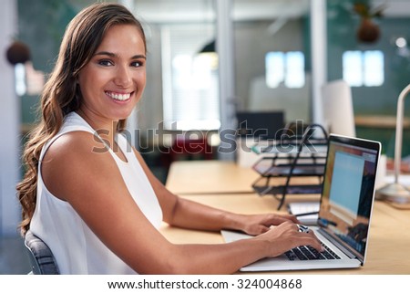 portrait of beautiful young business woman working on laptop computer at office desk