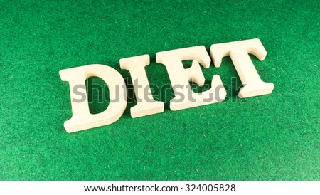 Alphabet letter DIET wooden block on green grass carpet. Concept of dieting. Isolated over the white background. Slightly defocused and close up shot. Copy space.