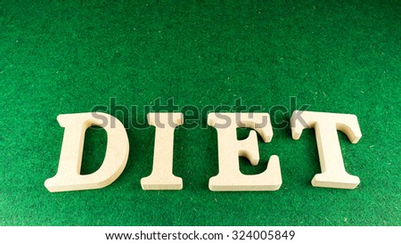 Alphabet letter DIET wooden block on green grass carpet. Concept of dieting. Isolated over the white background. Slightly defocused and close up shot. Copy space.