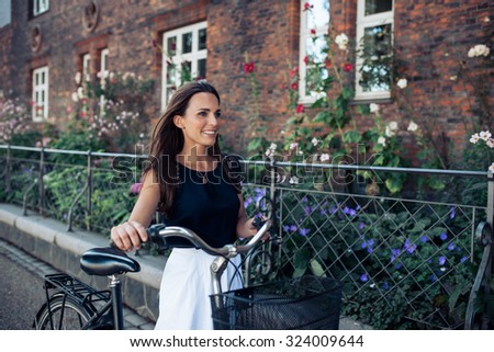 Portrait of beautiful young woman walking along the road with a bicycle. Woman with bike walking down the street in the city.