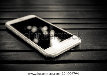 Smart phone with blank screen lying on wooden table- black and white filter effect
