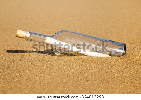 Message in a clear glass corked bottle partially buried in beach sand conceptual of a love letter from a sweetheart or plea for help form a shipwreck or marooned sailor carried ashore by the tides.