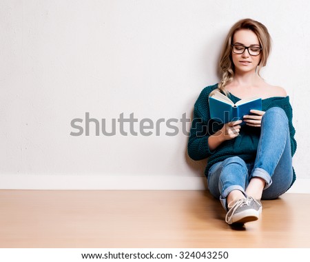 Young blonde woman relaxing on floor at home reading book.  Royalty-Free Stock Photo #324043250