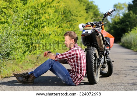 young man sitting on the road in addition the motorcycle