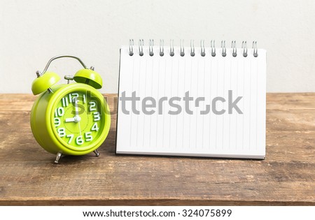 notebook with blank page and green clock on wood floor and cement background