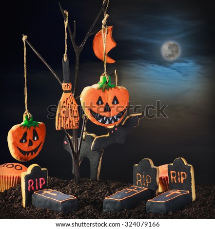 Halloween cookies hanging on a tree in the night sky. Focus on the graves on the ground