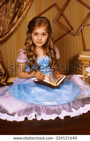 Little girl in a blue dress on the floor in room reading a book