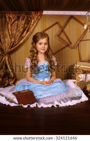 Little girl in a blue dress on the floor in room beside her is a book