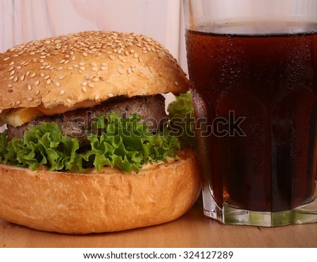 Big tasty appetizing fresh burger of green lettuce bacon slice meat cutlet and white bread bun with sesame seeds on wooden table and cola, horizontal picture