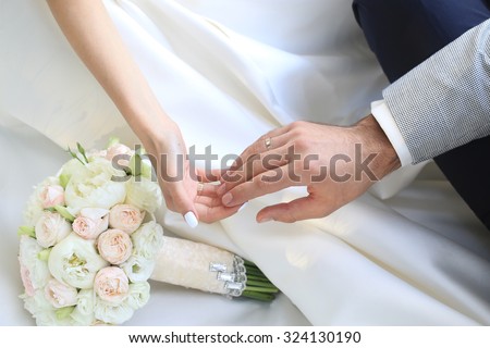 Beautiful fresh soft wedding decorative bouquet of white peony and rose flowers lying on dress of bride with female and male hands closeup, horizontal picture