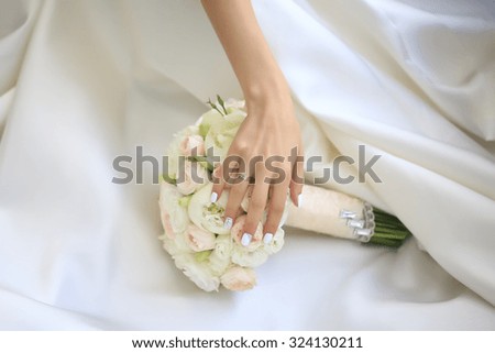 Beautiful fresh soft wedding decorative bouquet of white peony and rose flowers lying on dress of bride with female hand closeup, horizontal picture