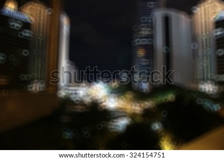 Blurry image of high rise building at night with round bokeh effect. Image suitable for background purpose and contain noise due to high ISO used.

