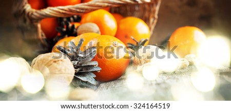 Christmas Light with Basket of Festive Food, Fruits and Nuts. Tangerines, Pine cones, Walnuts, Almonds are scattered on wooden background