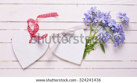 Background with fresh tender blue flowers and decorative hearts on white painted wooden planks. Selective focus. 
