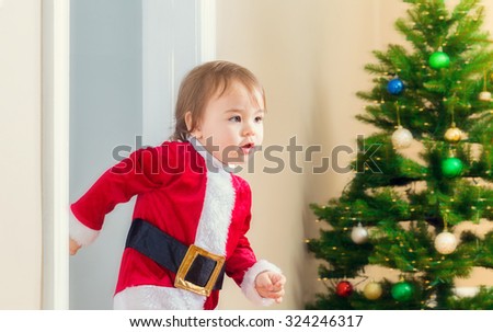 Little toddler girl in a santa suit dashing to open her Christmas presents