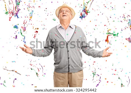 Joyful senior gentleman standing in a bunch of confetti streamers isolated on white background