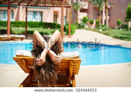 Young beautiful smiling woman faceless swimmer relax on a lounger by the summer pool. Royalty-Free Stock Photo #324364253
