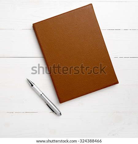 brown notebook and pen on white table view from above