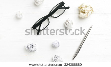 crumpled paper and eyeglasses with pen over white table