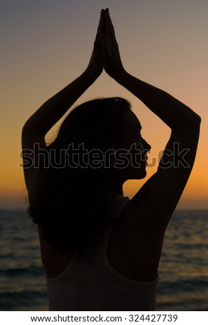 Young woman  practicing yoga at sunset by the sea