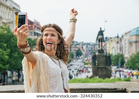 Happy young brunette bohemian woman tourist making selfie in the historical center of Prague. In the background Saint Wenceslas statue on Wenceslas Square in Prague. Tourism travel concept.