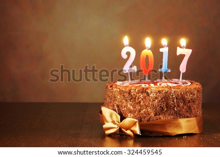 New Year 2017 still life. Chocolate cake and burning candles on brown background Royalty-Free Stock Photo #324459545