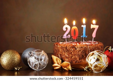 New Year 2017 still life. Chocolate cake and decorative tree balls with burning candles on brown background Royalty-Free Stock Photo #324459551
