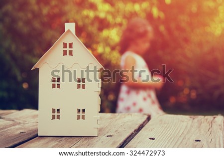 small house model over wooden table outdoors at garden and kid playing. selective focus
