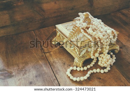 A beautiful antique golden jewelry box with natural white pearls on wooden table. retro filtered image
