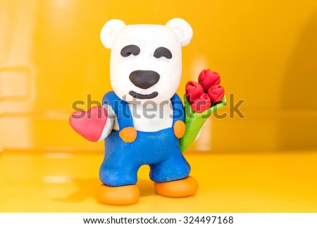 Cute white bear made out of play dough with a bouquet of roses in left hand and red heart on the right hamd