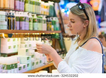 Young woman choosing cosmetic cream in beauty shop. Royalty-Free Stock Photo #324532202