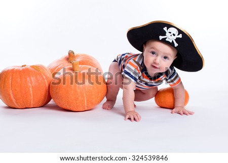 Beautiful baby in a striped T-shirt and a pirate hat on a white background sits next to pumpkins, picture with depth of field