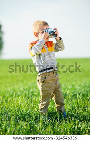 Little boy with an old camera shooting outdoor. Kid taking a photo using a vintage retro film cam. Green summer field.