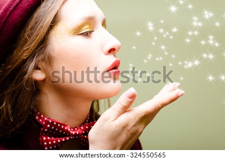 Picture of elegant beautiful girl in hat and bow tie sending air kiss. Side view of young pretty lady with flying lights on olivine abstract background.