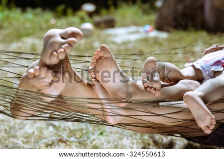 Picture of man and children legs barefoot. Closeup of happy family lying on hammock on sunny countryside background.