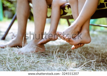 Picture of man and children legs barefoot. Closeup of happy family sitting on garden swing on sunny countryside background.