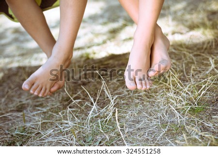 Picture of two children legs barefoot. Closeup of happy kids sitting and crossing legs on sunny countryside background.