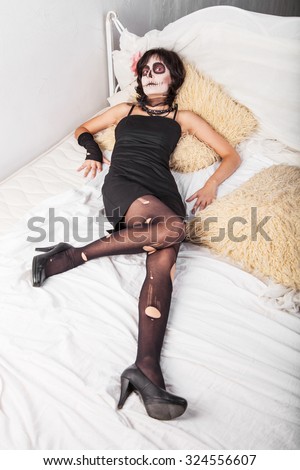 Young woman in costume and make-up for Halloween lying on the bed