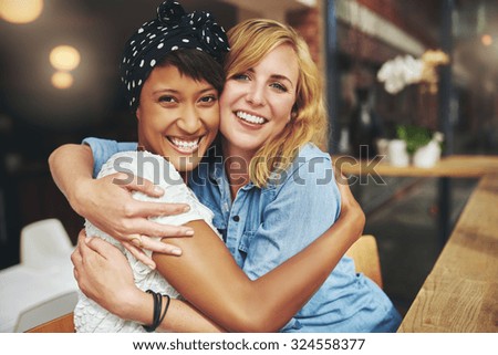 Two happy affectionate young woman hugging each other in a close embrace while laughing and smiling, young multiracial female friends Royalty-Free Stock Photo #324558377