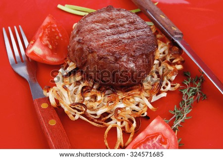 grilled beef fillet medallions on noodles with red hot chili pepper on red plate over wood table