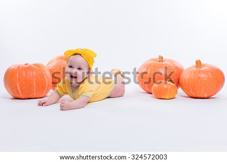 pretty baby girl in a yellow body with a yellow bow on her head lying on his stomach on a white background including pumpkins, picture with depth of field