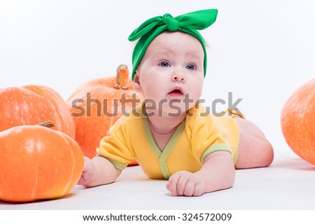 beautiful baby girl in a yellow body with green bow on her head lying on his stomach on a white background including pumpkins, picture with depth of field
