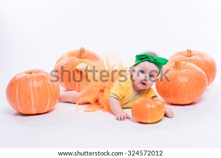beautiful baby girl in a yellow body with green bow on her head lying on his stomach on a white background including pumpkins, picture with depth of field