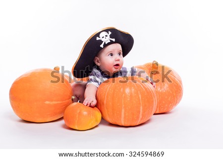 Cute baby with a pirate hat on his head lying on his stomach on a white background including pumpkins on Halloween, picture with depth of field