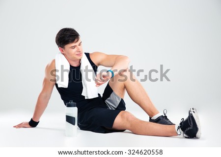 Portrait of a happy athletic man resting on the floor and looking on fitness tracker isolated on a white background