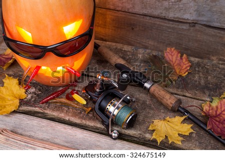 halloween pumpkin head in eyeglass with fishing tackles on wooden boards background
